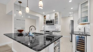 Una cucina moderna con isola centrale, mobili bianchi, forno a microonde integrato e cantinetta per vini.
