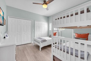 Une chambre avec un lit superposé, un lit simple, un ventilateur de plafond et une porte double blanche.