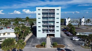 Un hôtel à plusieurs étages, doté d’une entrée principale et entouré d’un parking et de palmiers.