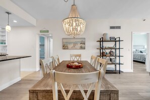 Un coin repas avec une table en bois, des chaises, un lustre et une bibliothèque.