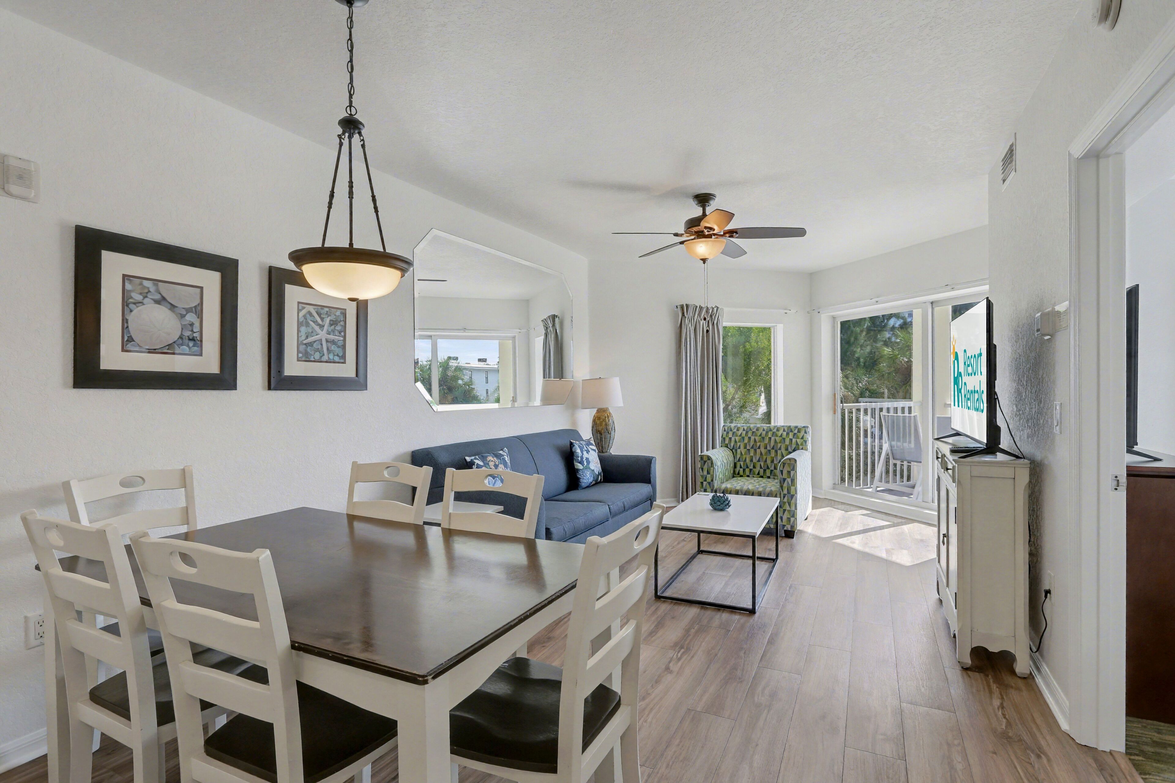 A spacious living area with a dining table, white chairs, a blue sofa, and a ceiling fan.