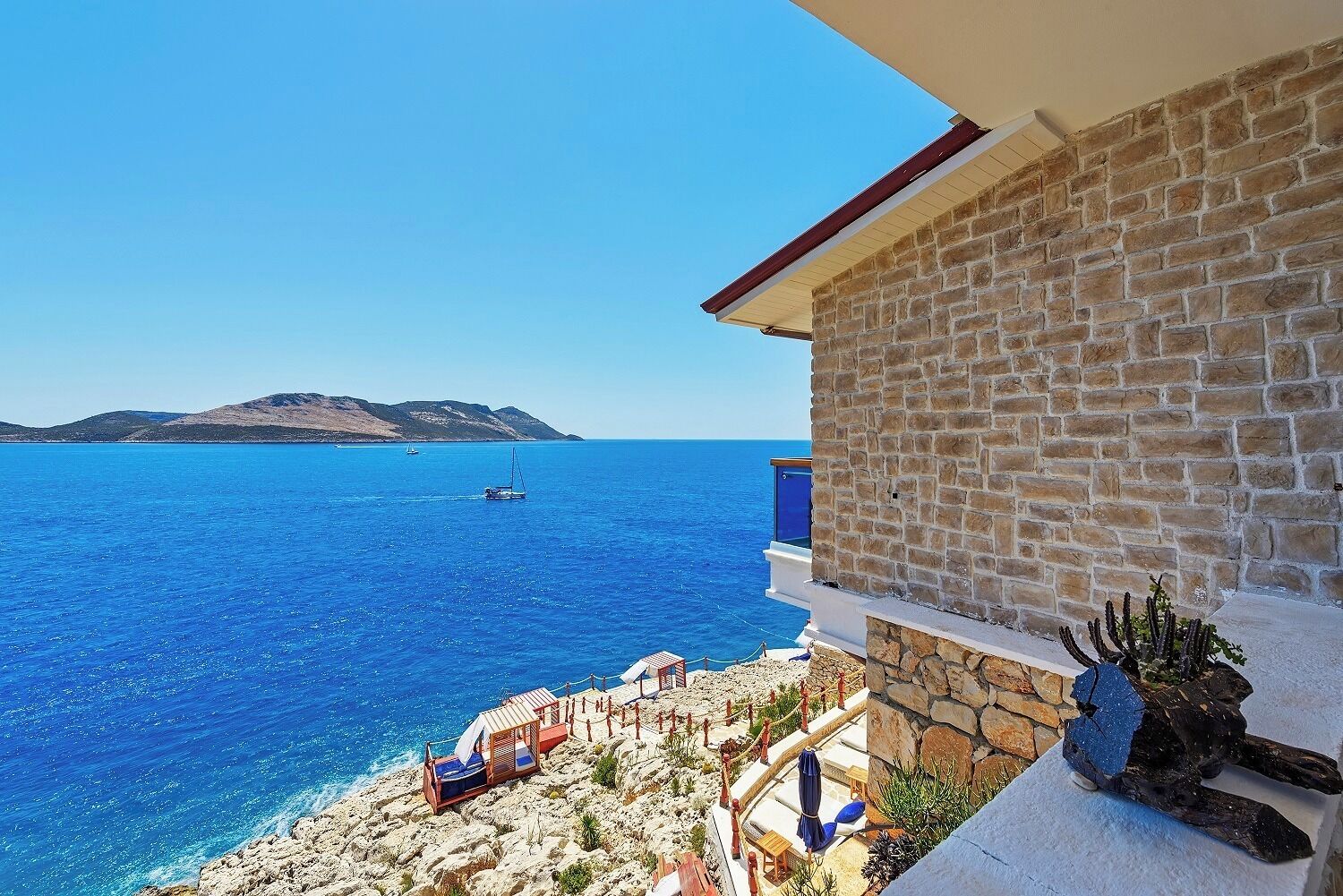 A balcony with a stone wall, a view of the sea, and a small garden area with a cactus sculpture.