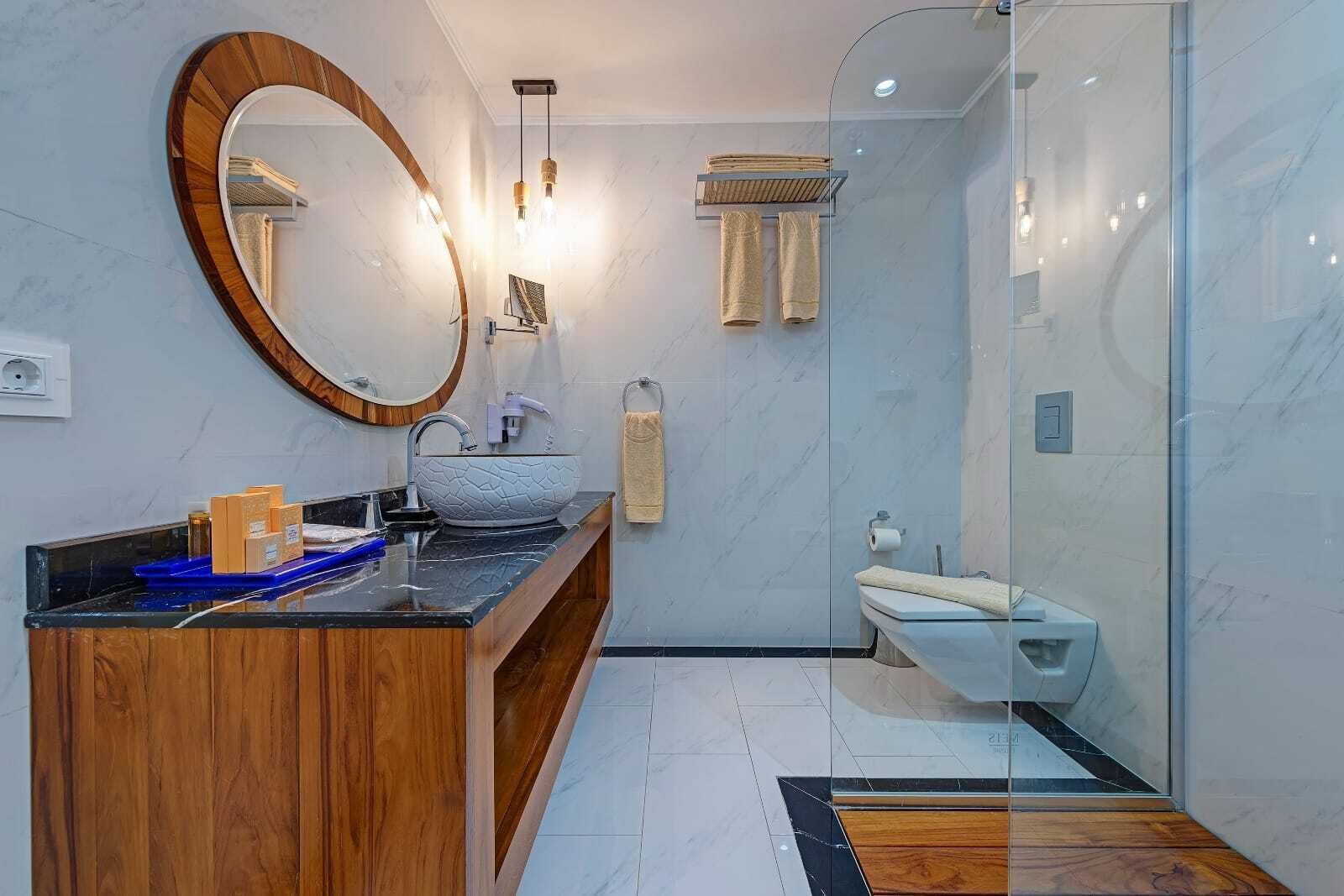 A modern bathroom with a wooden vanity, a round mirror, a vessel sink, and a glass shower enclosure.