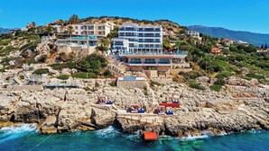 A coastal hotel with multiple floors, a rocky shoreline, and clear blue waters. - Meis Exclusive Hotel (Kas)