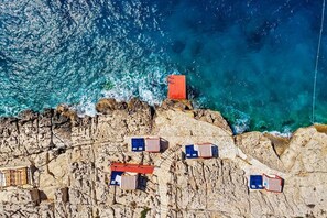 An aerial view of a coastal area with rocky terrain and several small structures, possibly beach huts, along the cliffside. - Meis Exclusive Hotel (Kas)