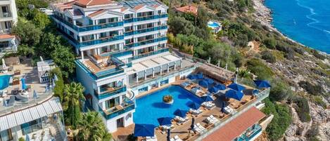 Un hotel de varios pisos con piscina en la azotea y balcones con vistas a la costa.
