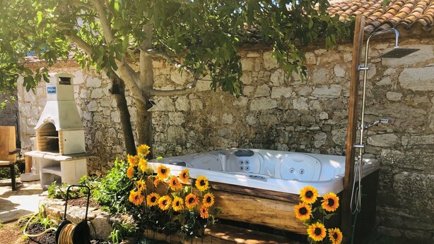 Un muro in pietra, una panchina di legno, una vasca idromassaggio e girasoli.