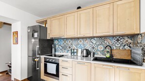 Una cucina con mobili in legno, un frigorifero in acciaio inossidabile, un forno nero e uno schienale piastrellato.