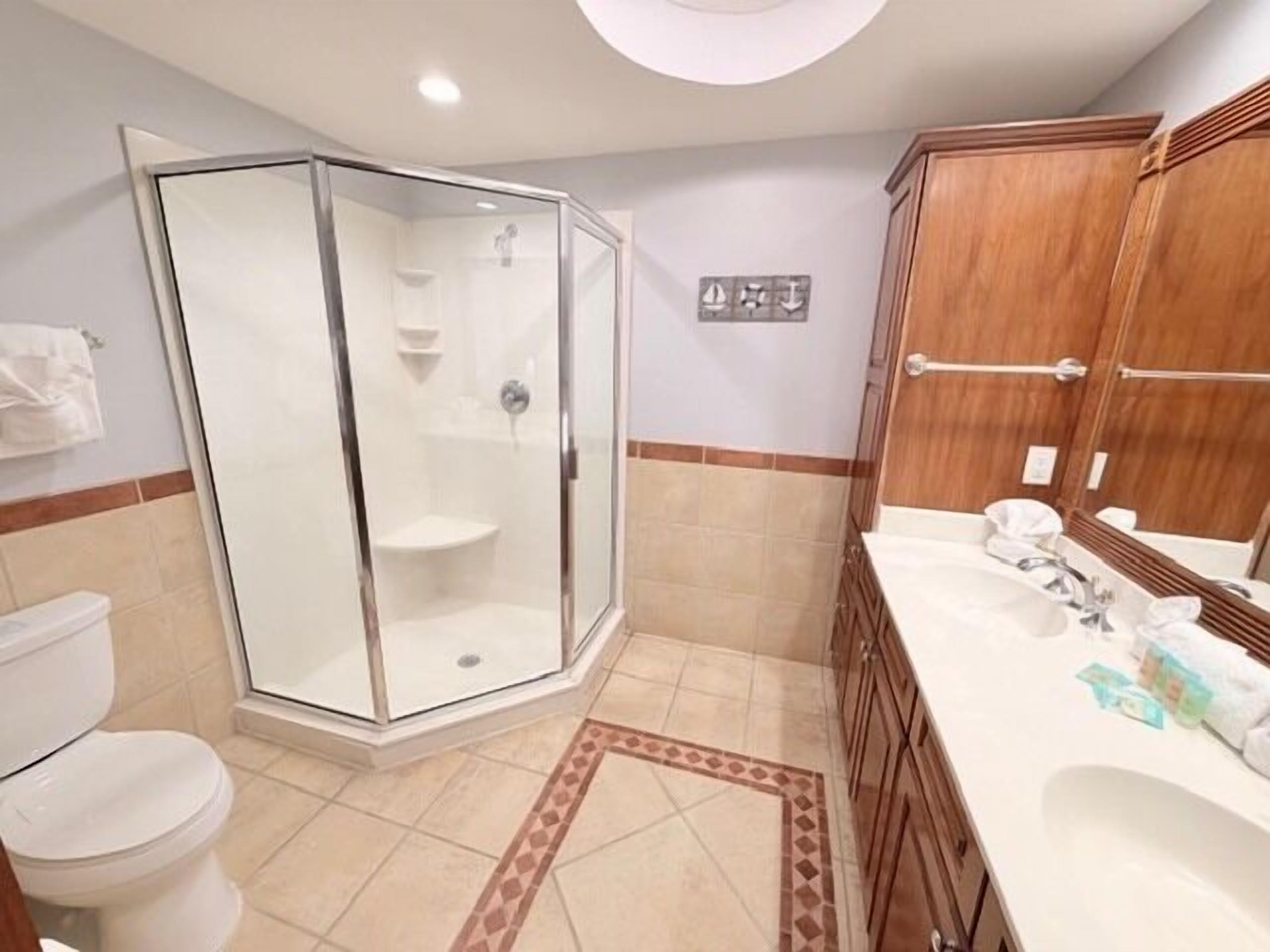Ett badrum med en dusch som är avskärmad med glasväggar, en toalett, ett handfat och träskåp.