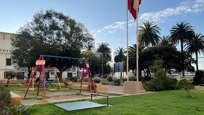 A playground with swings and a green mat, surrounded by grass and palm trees. - Oceana Suites Valparaíso Yungay (Valparaíso)