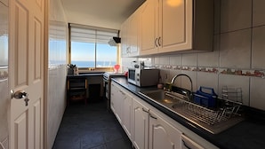 A kitchen with white cabinets, a microwave, a sink, and a window with a view. - Oceana Suites Valparaíso Yungay (Valparaíso)