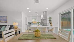 Cozinha moderna com armários brancos, geladeira de aço inoxidável e área de refeições com mesa e cadeiras de madeira.