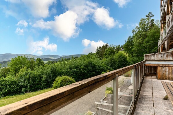 A balcony with a view of a forested hillside and distant mountains.