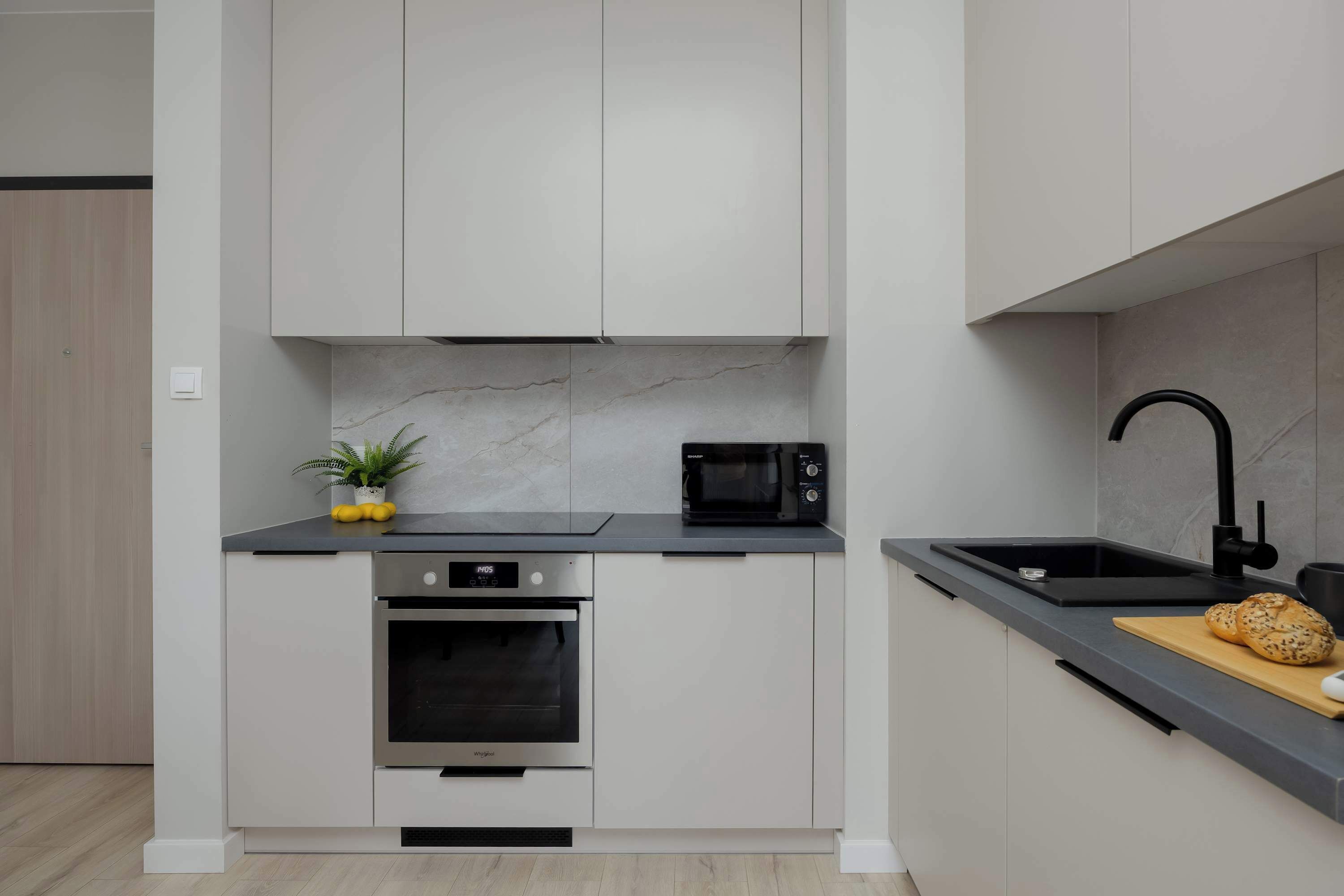 A modern kitchen with white cabinets, a built-in oven, a microwave, and a black faucet.