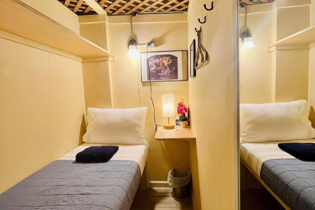 Ein kleiner, kompakter Raum mit zwei Einzelbetten, einem Schreibtisch mit Lampe und einer kleinen Mülleimer.