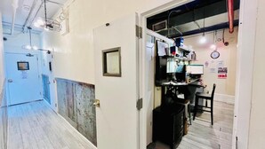 A hallway with a door leading to a room with a desk, chair, and various items on the wall. - New York Spirit Retreats HOSTEL (New York)