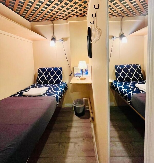 Une petite chambre, de taille modeste, comprenant deux lits simples, une petite table avec une lampe et une poubelle.