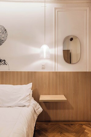 A bedroom with a bed, a bedside table, a wall-mounted mirror, and a hanging light fixture. - Metro Explorer near Hospital & Metro Baquedano (Providencia)