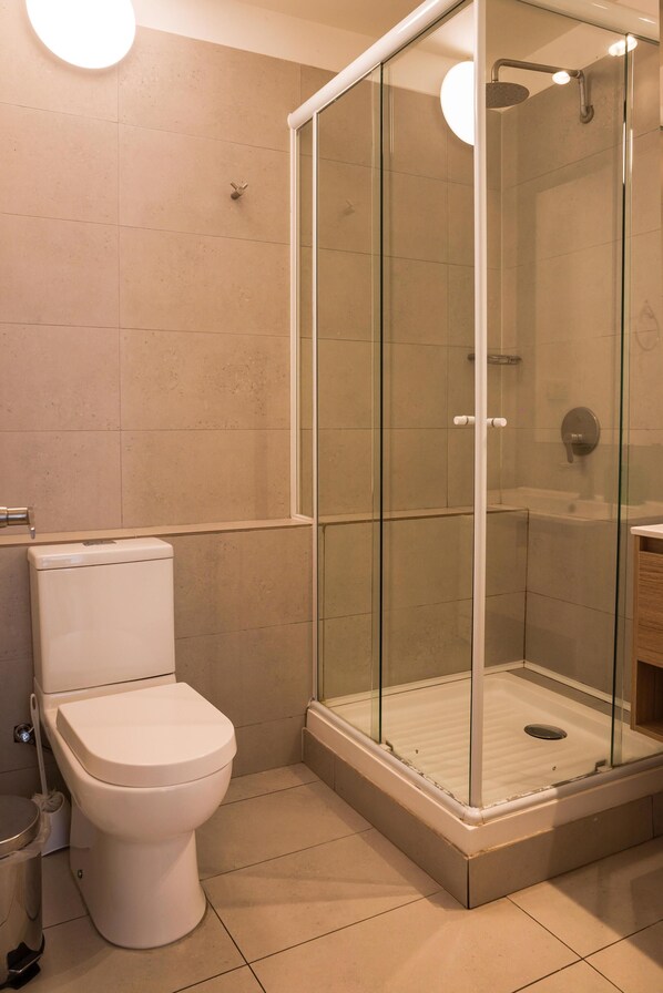 A bathroom with a glass-enclosed shower, a toilet, and a sink. - Elegant Studio | AC and Patio Perfect for Families (Providencia)