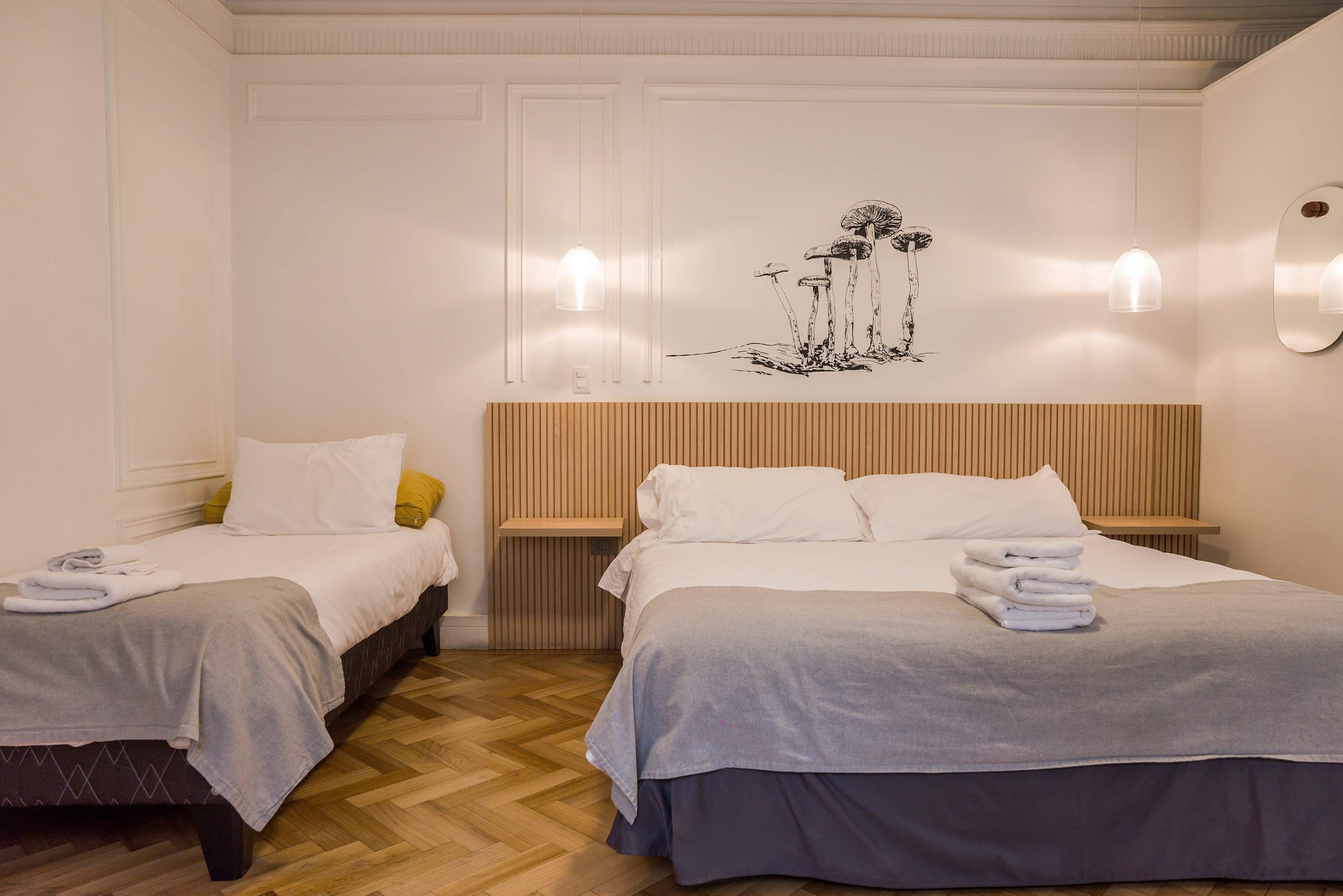 A hotel room with two beds, a wooden headboard, a wall-mounted artwork, and a bedside table with a lamp.