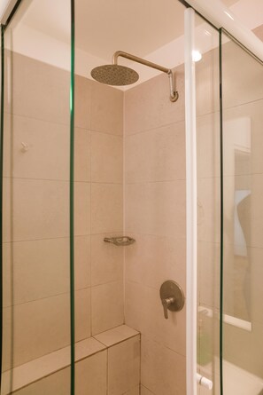 Eine begehbare Dusche mit Glaswänden, einer Handbrause, einer Bedienkonsole und einer Glastür.