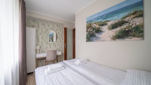 Une chambre d’hôtel avec un lit, un bureau, une chaise, un miroir et un tableau représentant une plage accroché au mur.