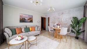 Un salon moderne avec un canapé gris, une table de salle à manger ronde entourée de chaises, une table basse agrémentée de fleurs et une grande plante.