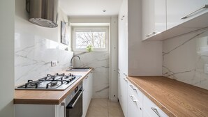 Une cuisine moderne dotée d’une cuisinière à gaz, d’un plan de travail en bois, de meubles blancs et d’une fenêtre donnant sur les arbres.
