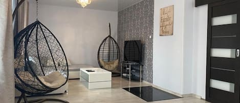 A modern interior with a hanging chair, a sofa, a small table, and a door with frosted glass panels.