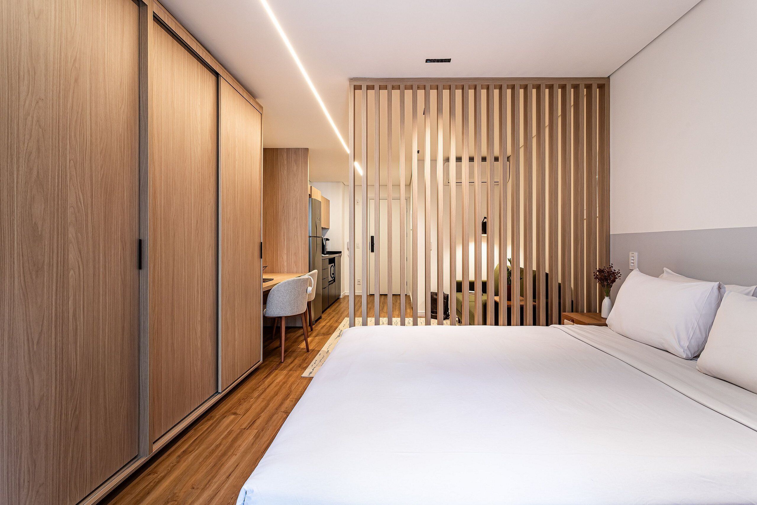 A modern bedroom with a large bed, wooden wardrobe, and a desk area.
