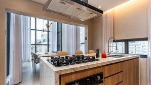 A modern kitchen with a central island, built-in oven, and a large window providing a view of the city. -  Pivô Alameda Franca by Viva - Conforto e Estilo nos Jardins (São Paulo)