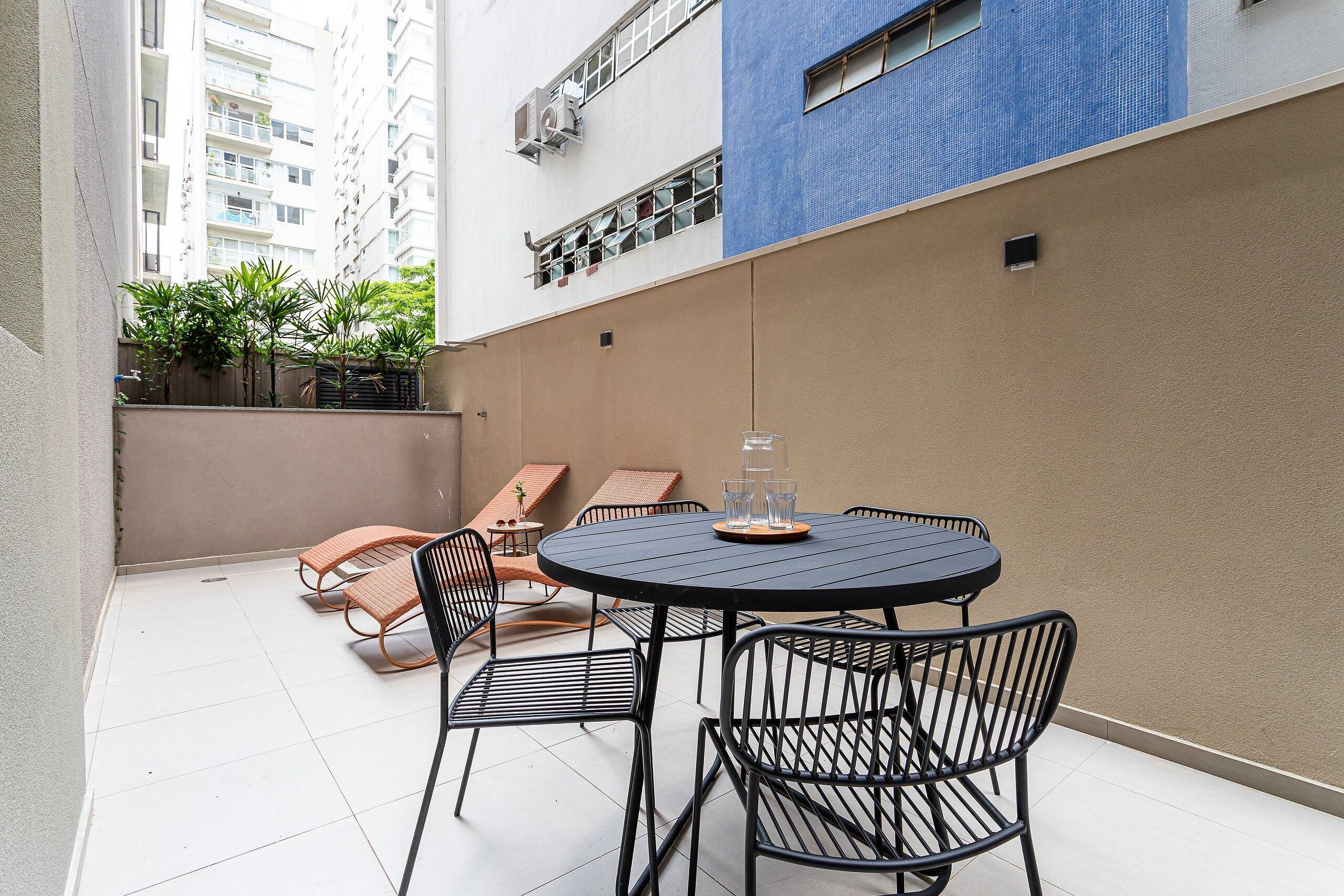 Un patio con una mesa redonda y sillas, una planta pequeña y vistas de un edificio de gran altura.