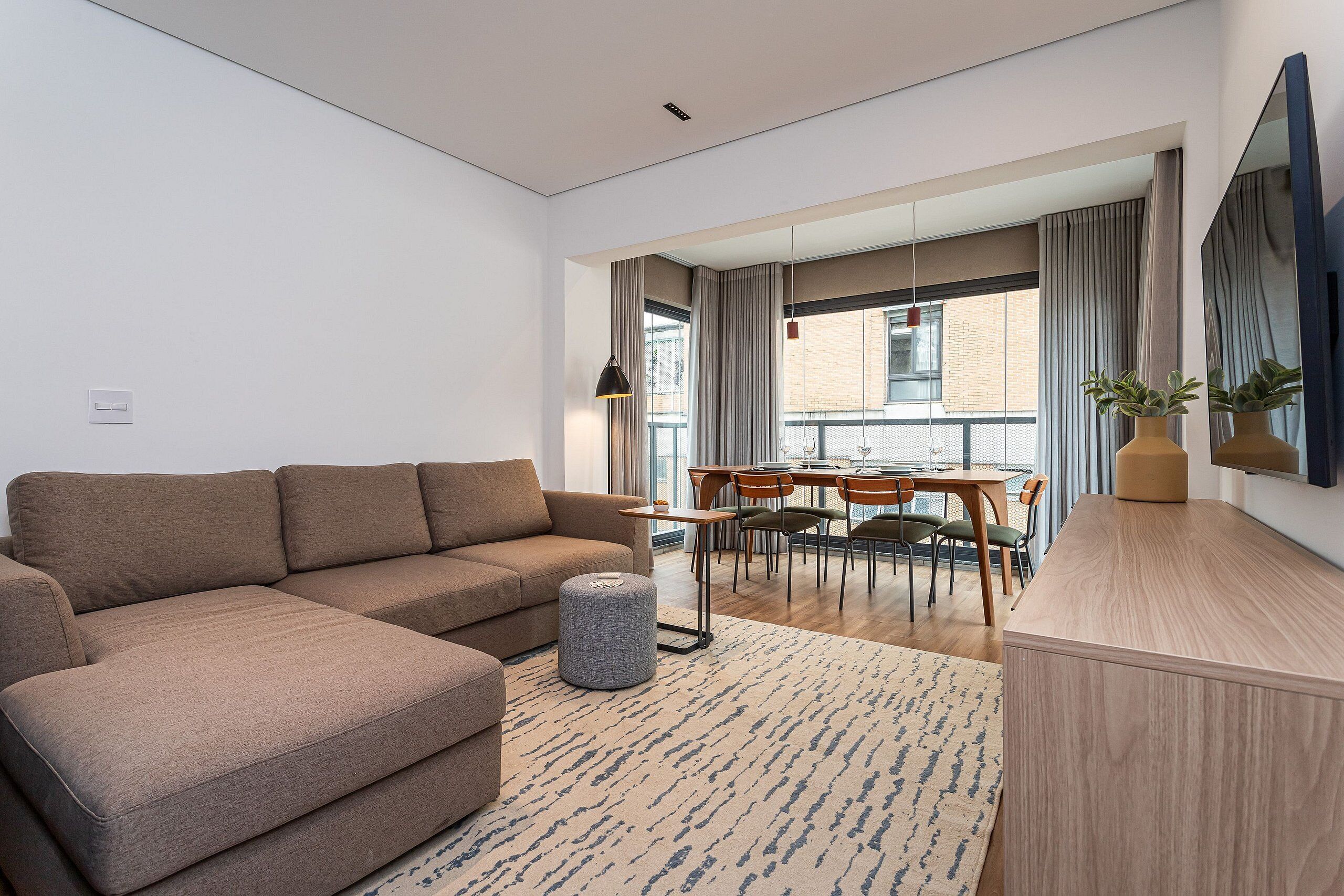 Un salon moderne comprenant un canapé, un pouf et un coin repas avec des chaises et une table.