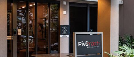 A hotel entrance with a modern design, a signboard, and a potted plant.