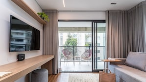 A modern living room with a flat-screen TV, a sofa, a coffee table, and a balcony with chairs. -  Pivô Alameda Franca by Viva - Conforto e Estilo nos Jardins (São Paulo)