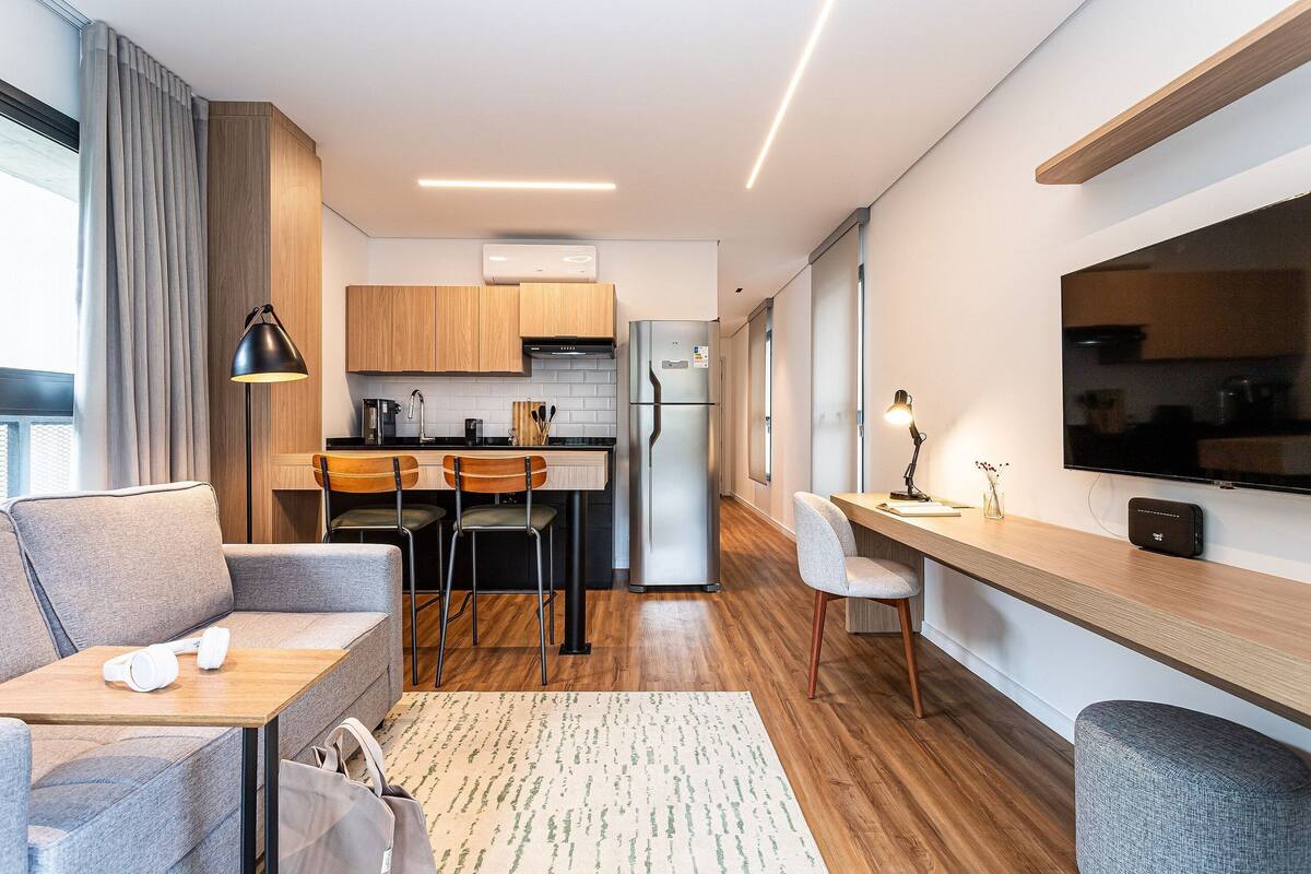 A modern kitchen with wooden cabinets, a refrigerator, a dining area with chairs, and a sofa.