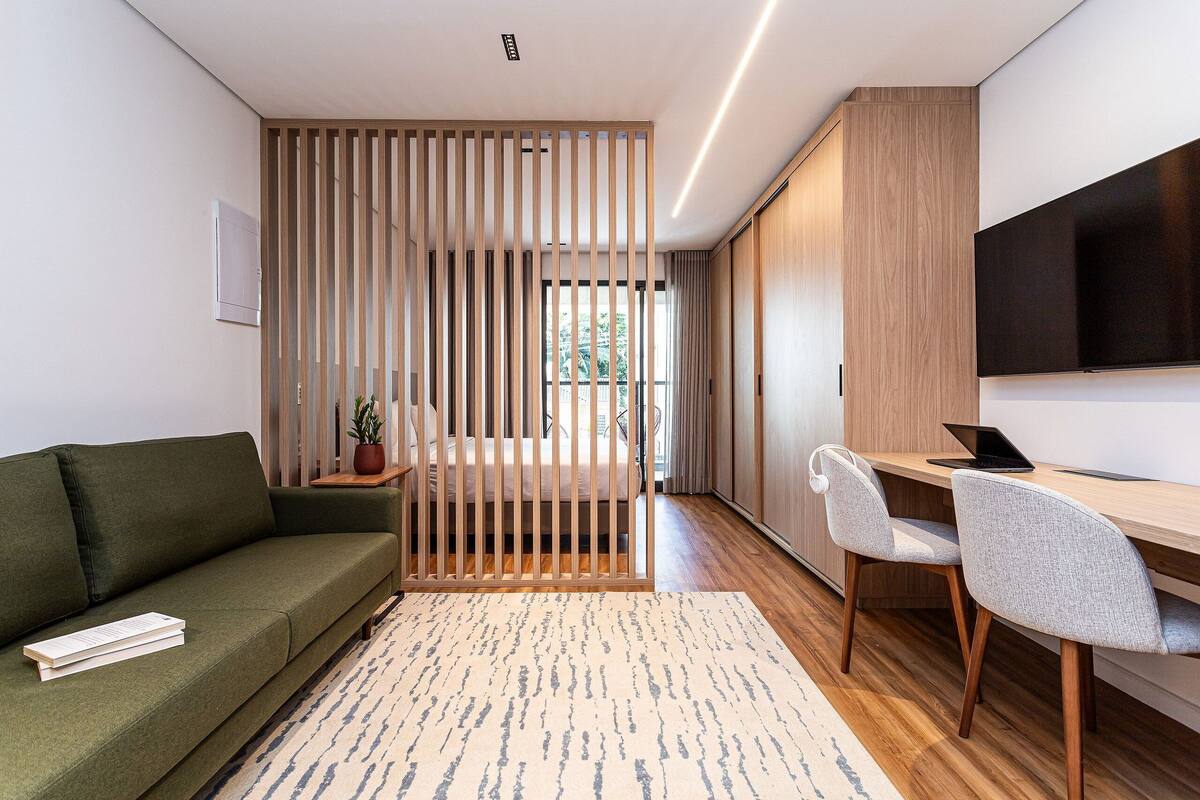 A modern room with a green sofa, a wooden desk with two chairs, a TV, and a sliding door.