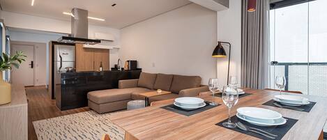 A modern living space with a dining area, kitchen, and a large window.