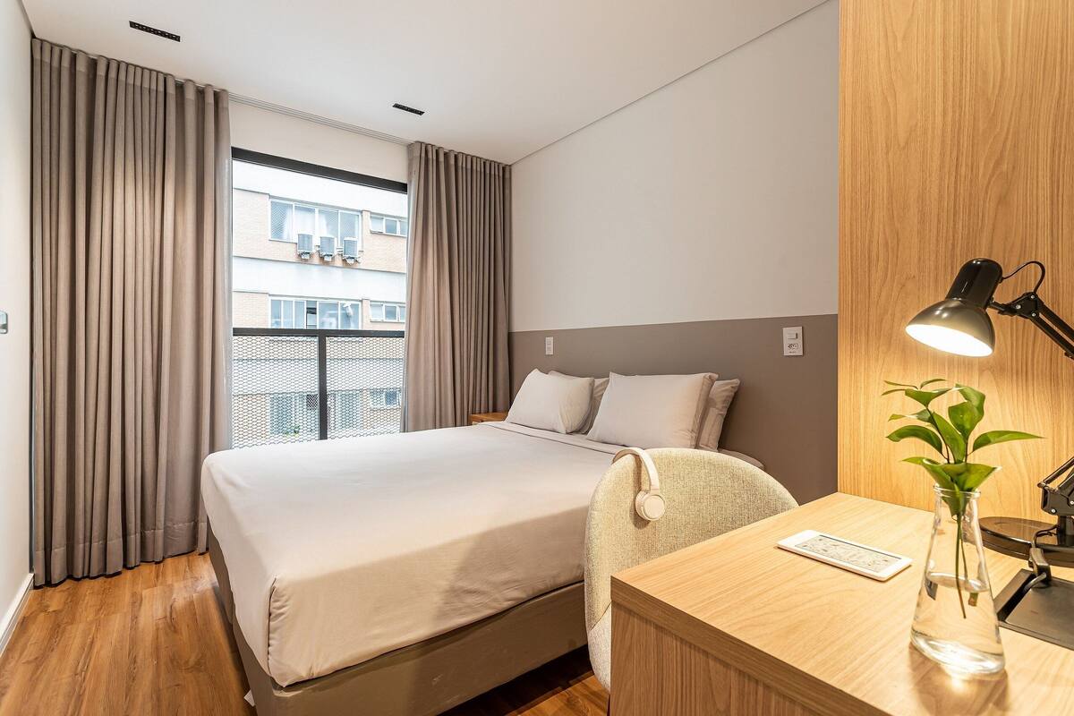A hotel room with a bed, a desk, a lamp, and a plant.
