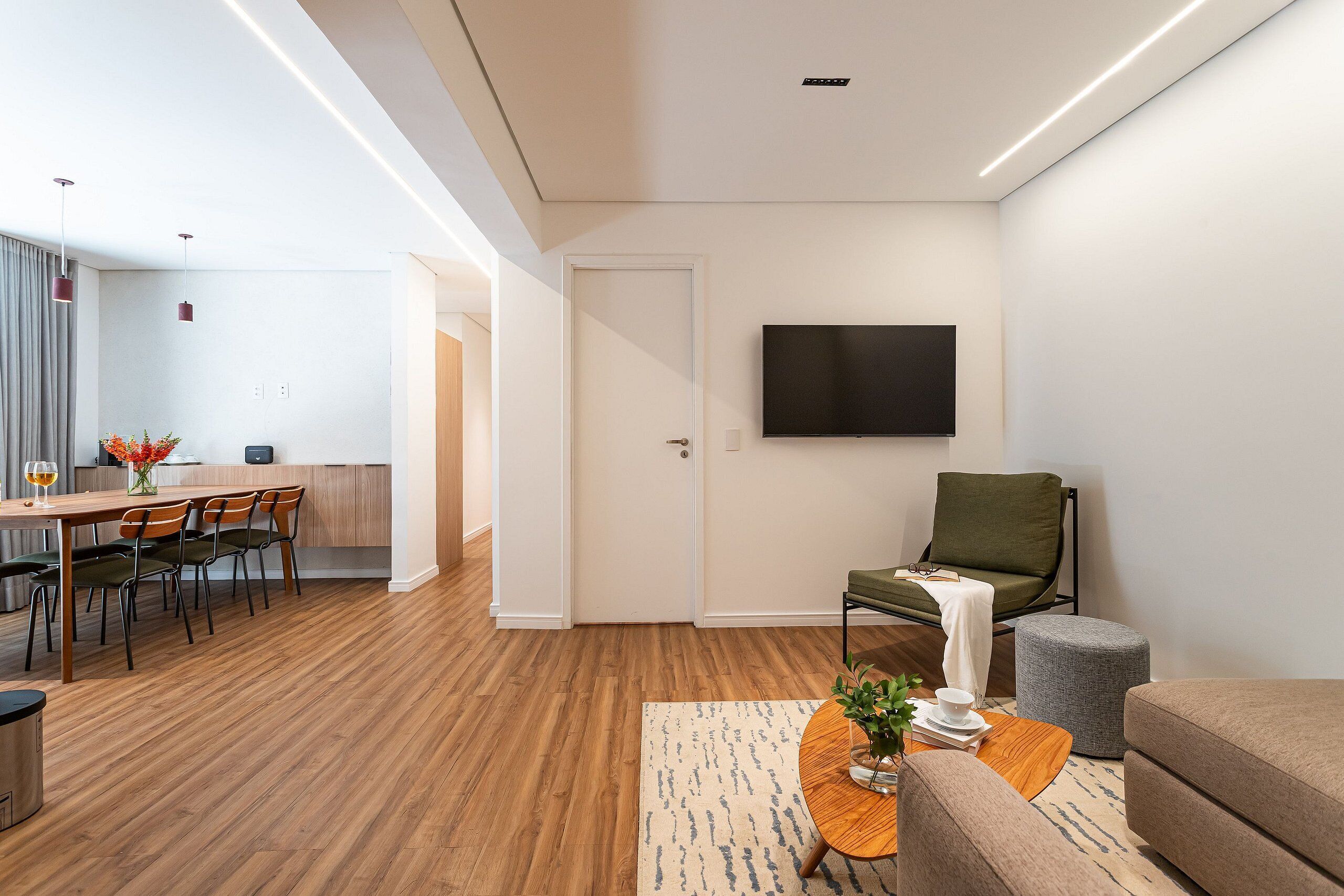 A modern living room with a dining area, a flat-screen TV mounted on the wall, and a green chair.