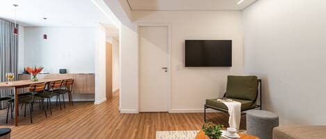 A modern living room with a dining area, a flat-screen TV mounted on the wall, and a green chair.