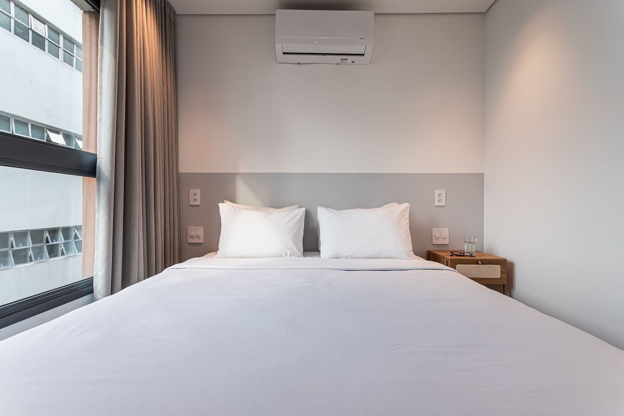 Een hotelkamer met een groot bed, twee kussens, een nachtkastje, een lamp en een airconditioner.