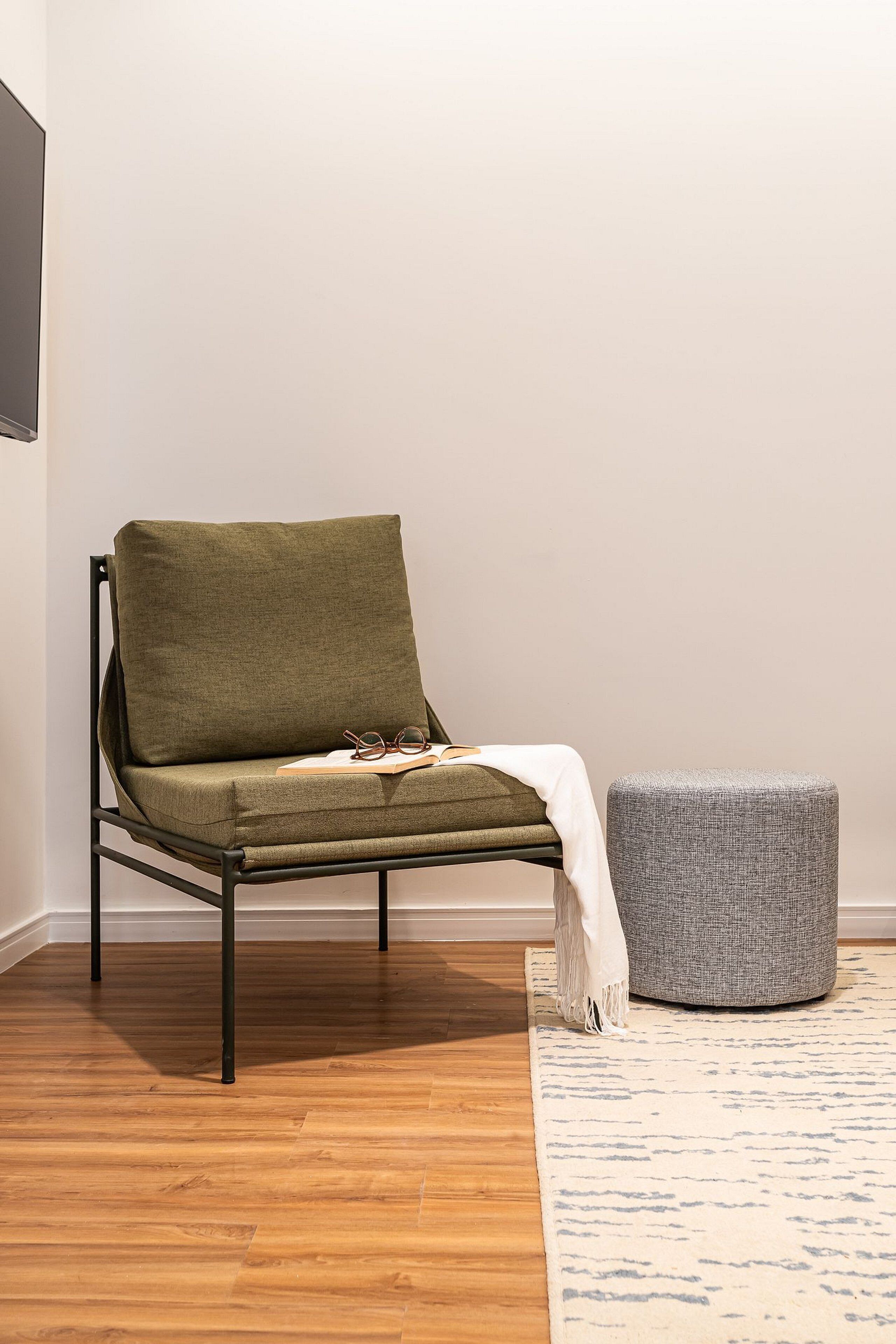 A modern room with a green sofa, a grey ottoman, and a patterned rug.