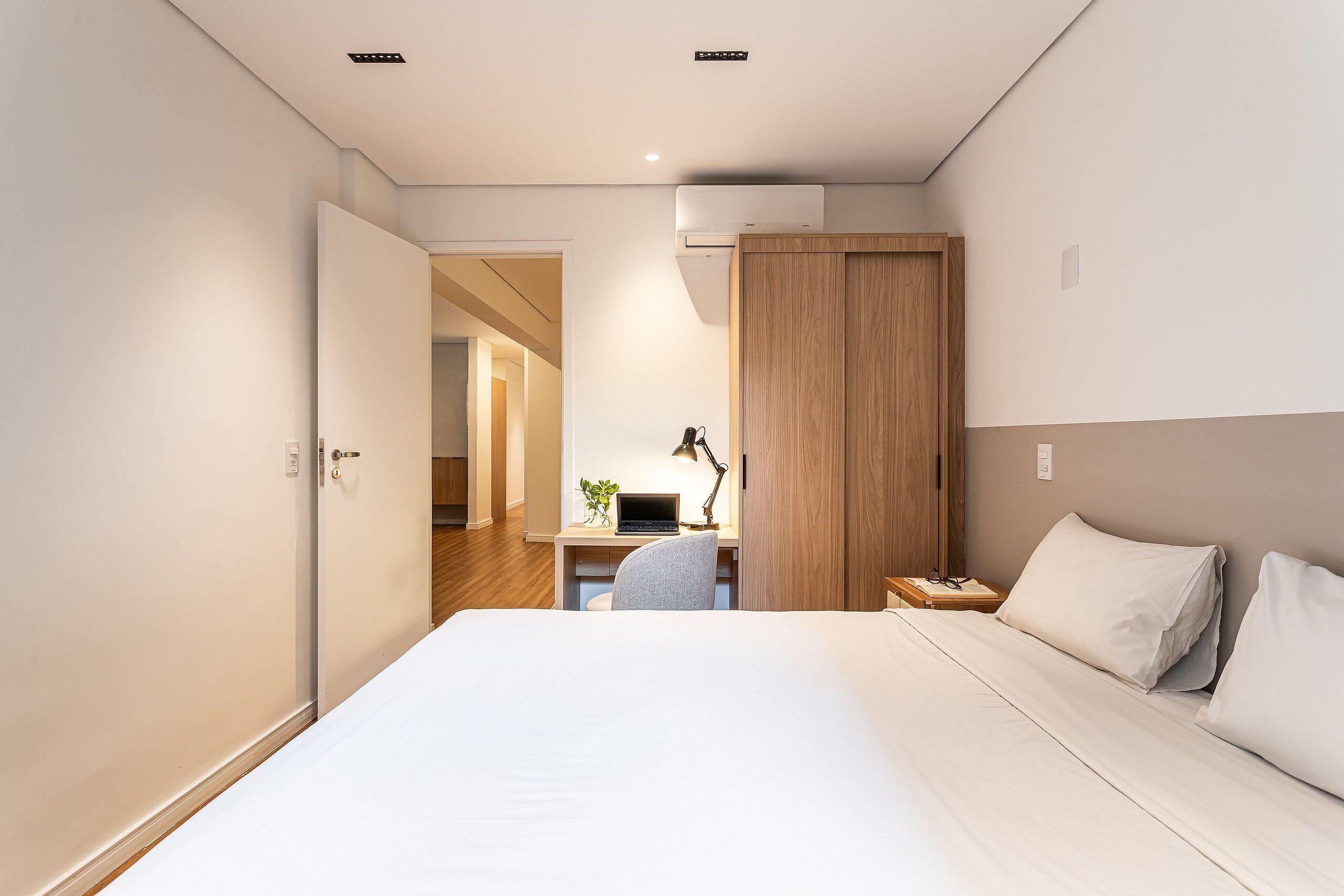A bedroom with a bed, a desk with a laptop, a chair, and a nightstand.