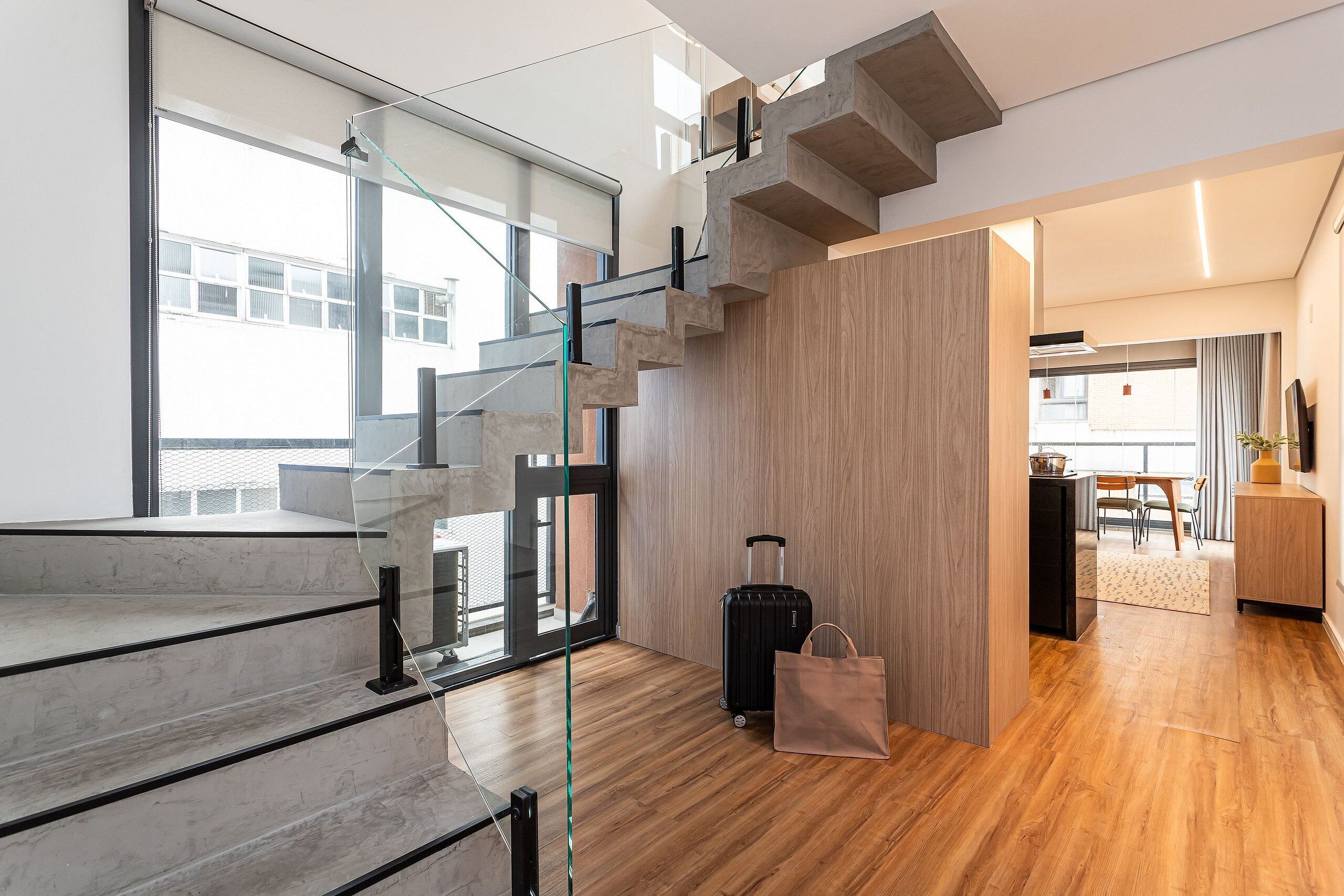 A modern interior with a staircase, a wooden floor, a glass door, and a bag.