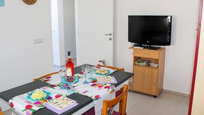 Un comedor con una mesa preparada para dos, un televisor sobre un mueble y una puerta que da a otra habitación.