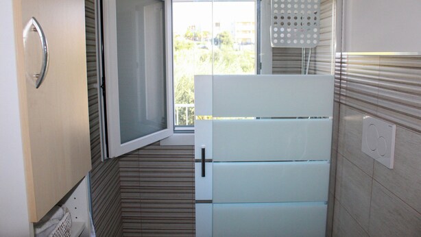 Una cocina compacta con refrigerador integrado, una ventana con persianas y un perchero.