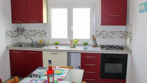 Una cocina compacta con armarios rojos, una estufa a gas y un lavavajillas.