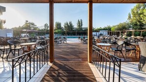 A covered outdoor area with wooden flooring, metal railings, and multiple tables and chairs arranged for dining or lounging. - Aegean Bay Hotel - All Inclusive (Marmari)