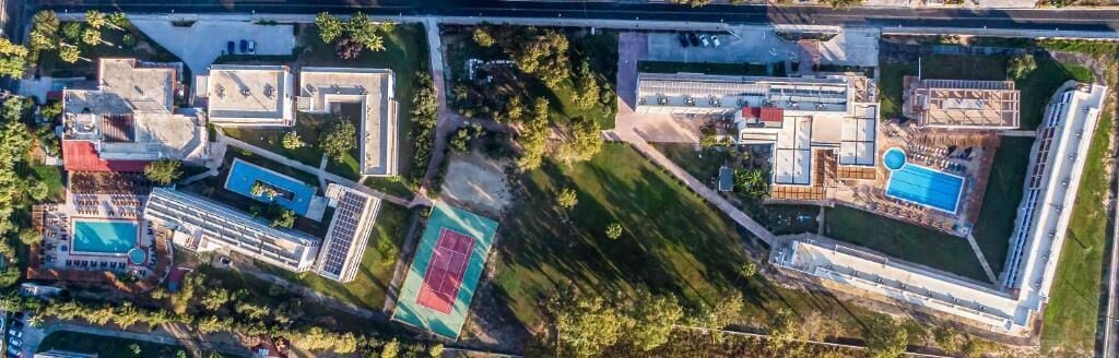 Oversigtsbillede af et resort med flere bygninger, en swimmingpool, tennisbaner og anlagte områder.